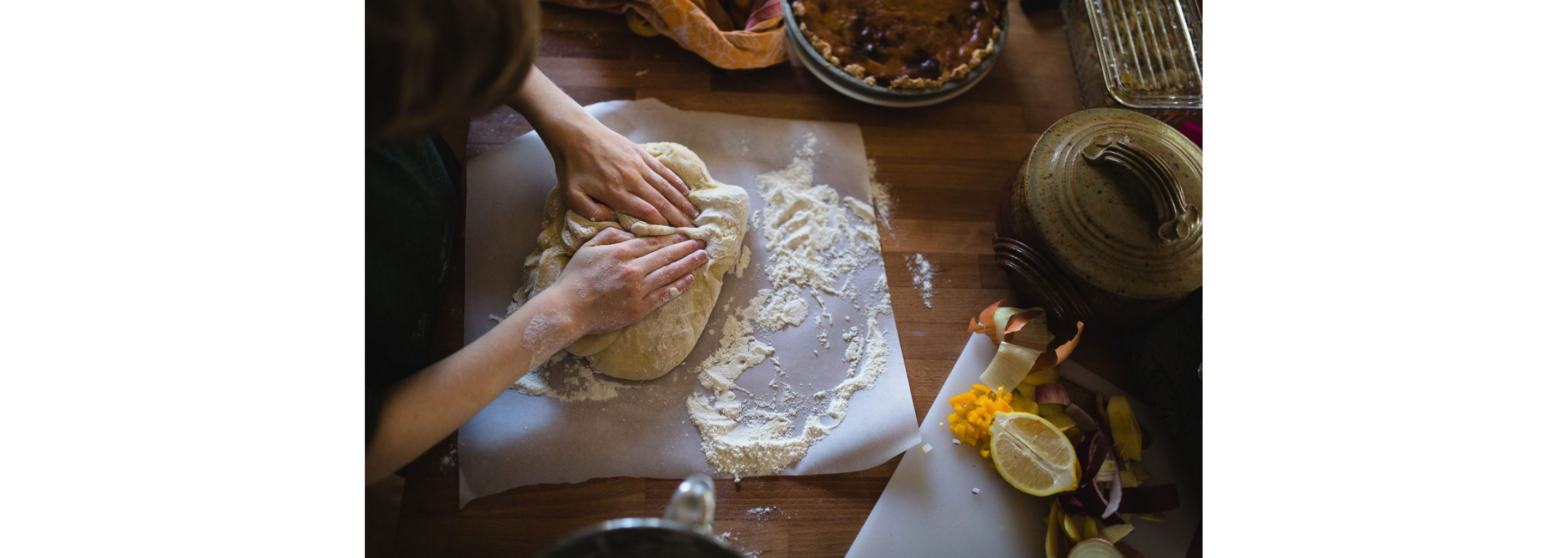 A person kneading dough with flour on a sheet of parchment paper.