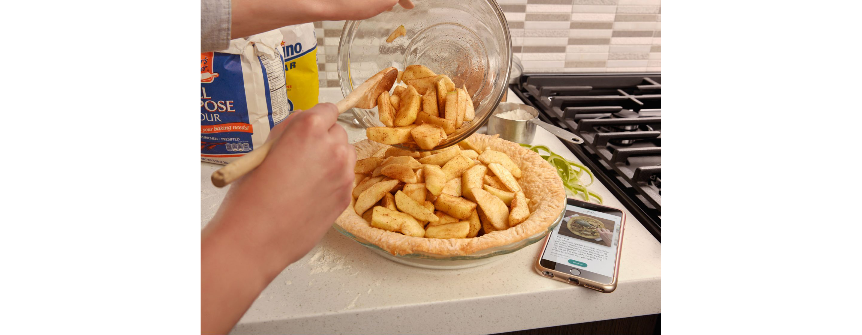 A person pouring apple slices into a pie crust in a glass dish.