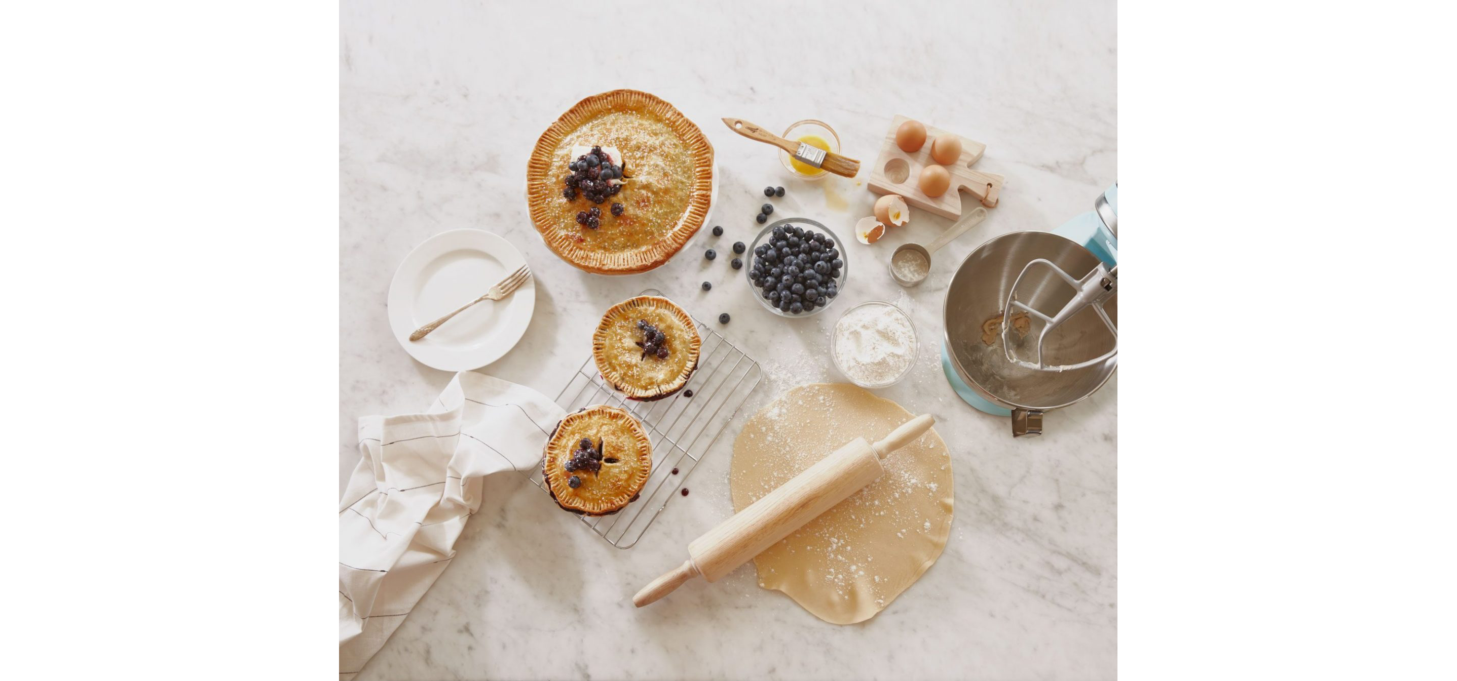 A set of three blueberry pies resting on a white kitchen counter.