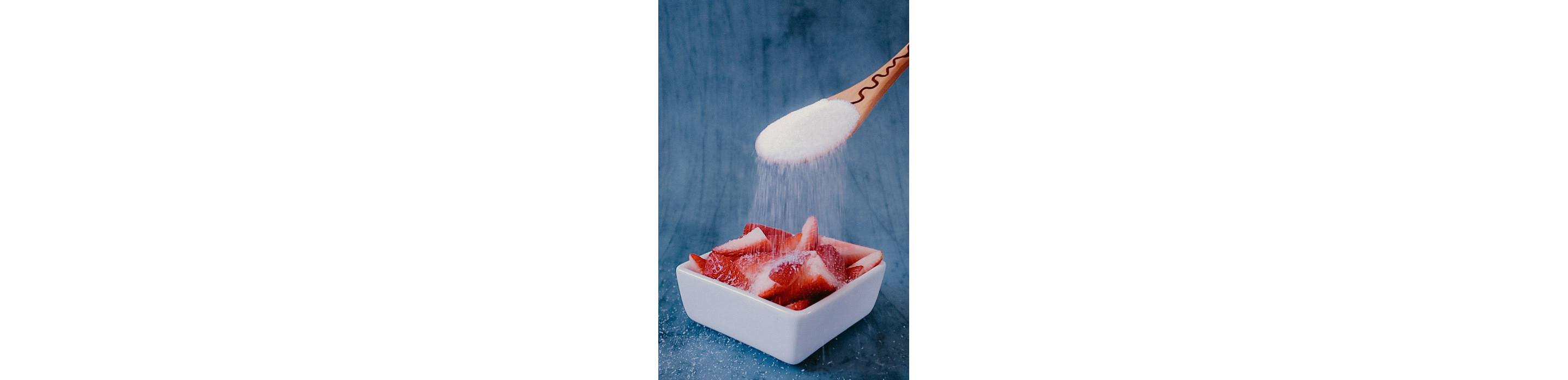 A wooden spoon pouring sugar over strawberries.