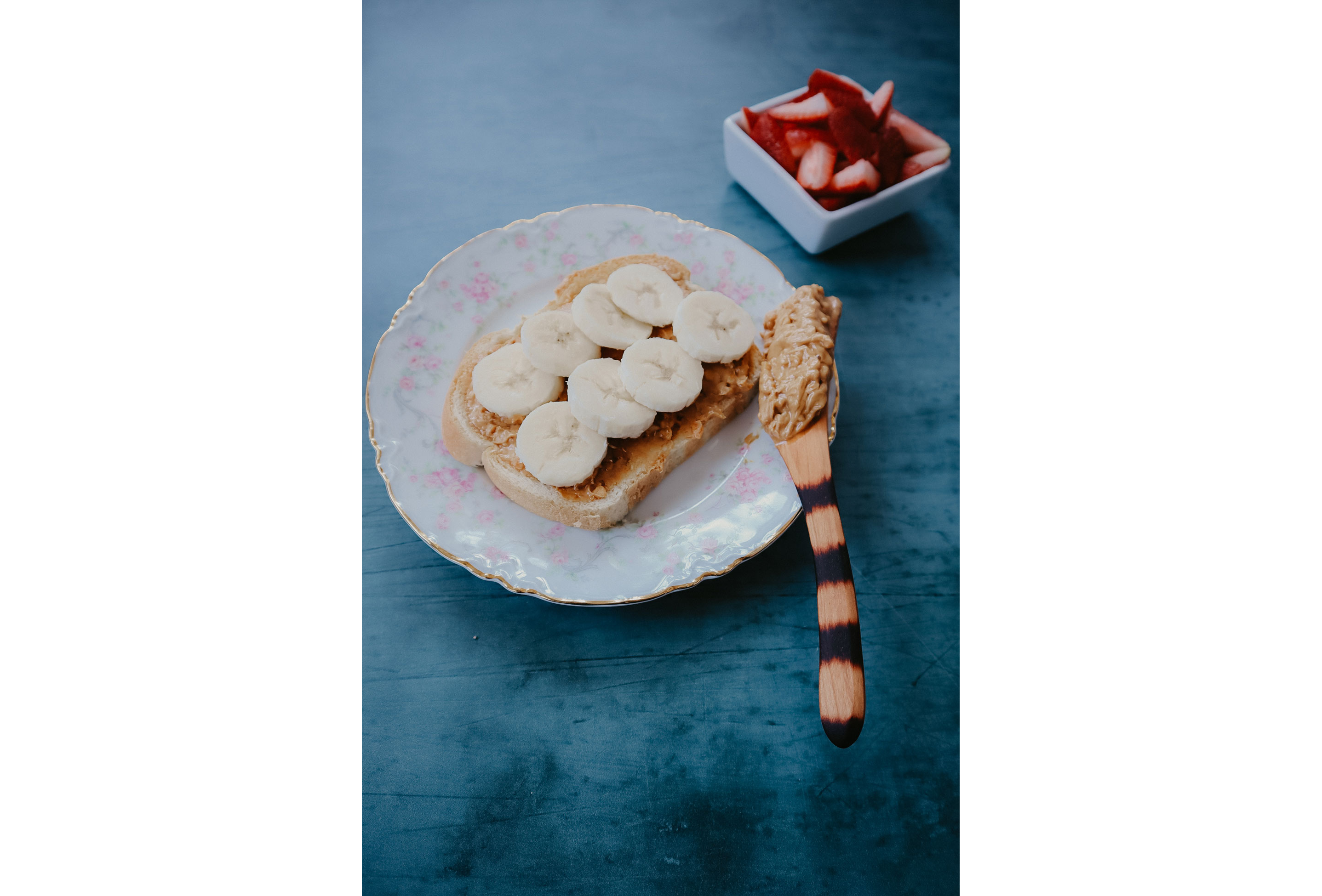 A wooden knife being used to spread peanut butter.
