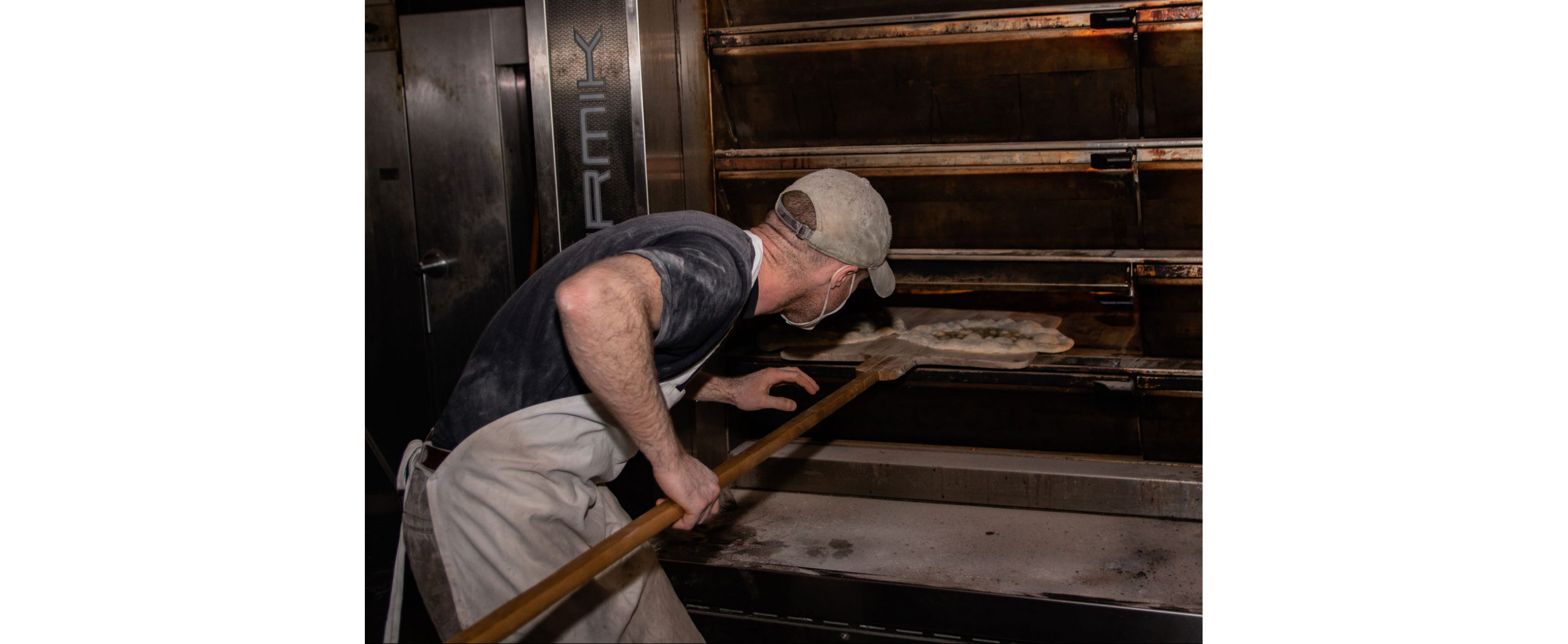 A baker placing pizzas in a large oven.