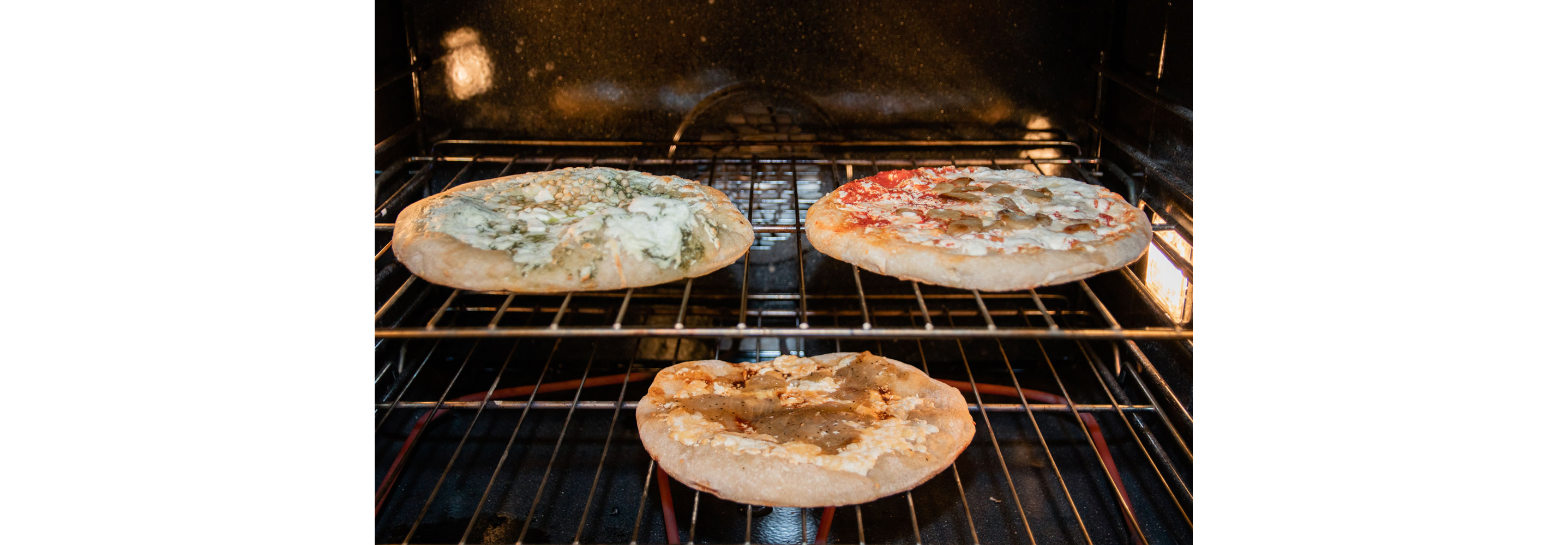 Three pizzas baking in a large oven.
