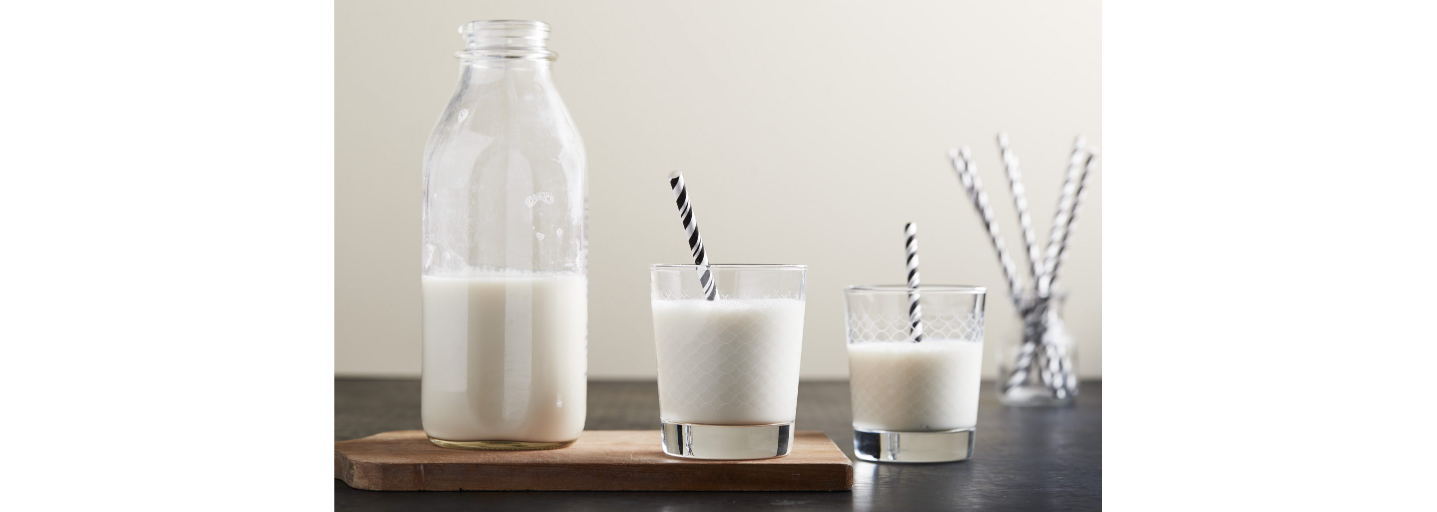 A glass jar of milk next to two to full glasses of milk.