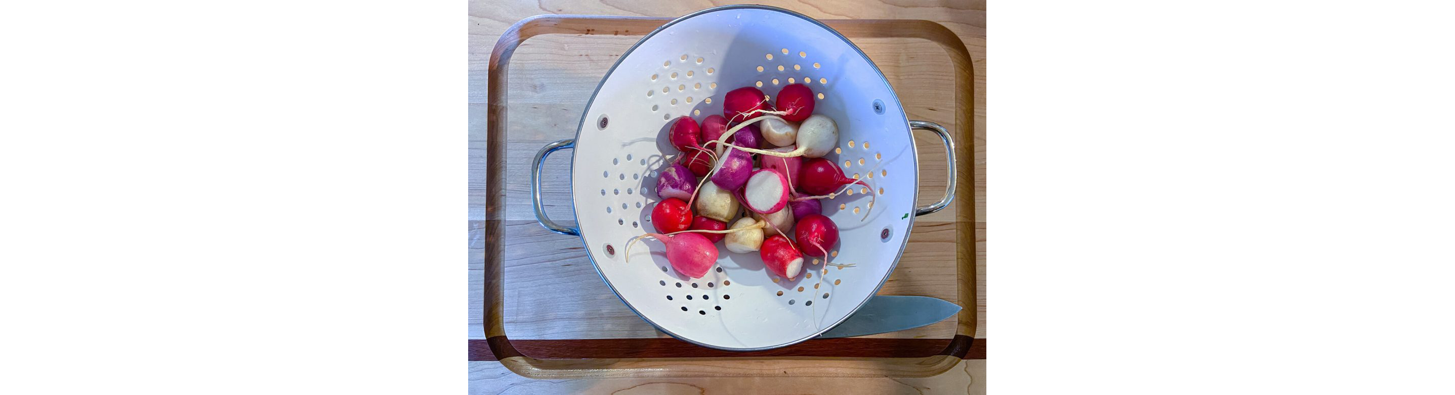 A metal strainer filled with freshly cleaned, whole radishes.
