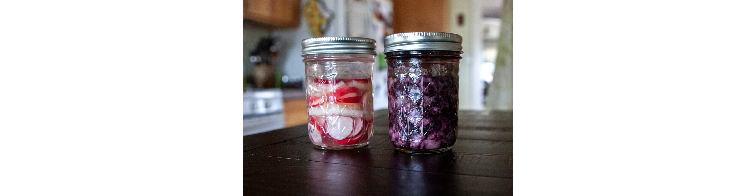 Two glass jars holding fermented radishes and red cabbage.