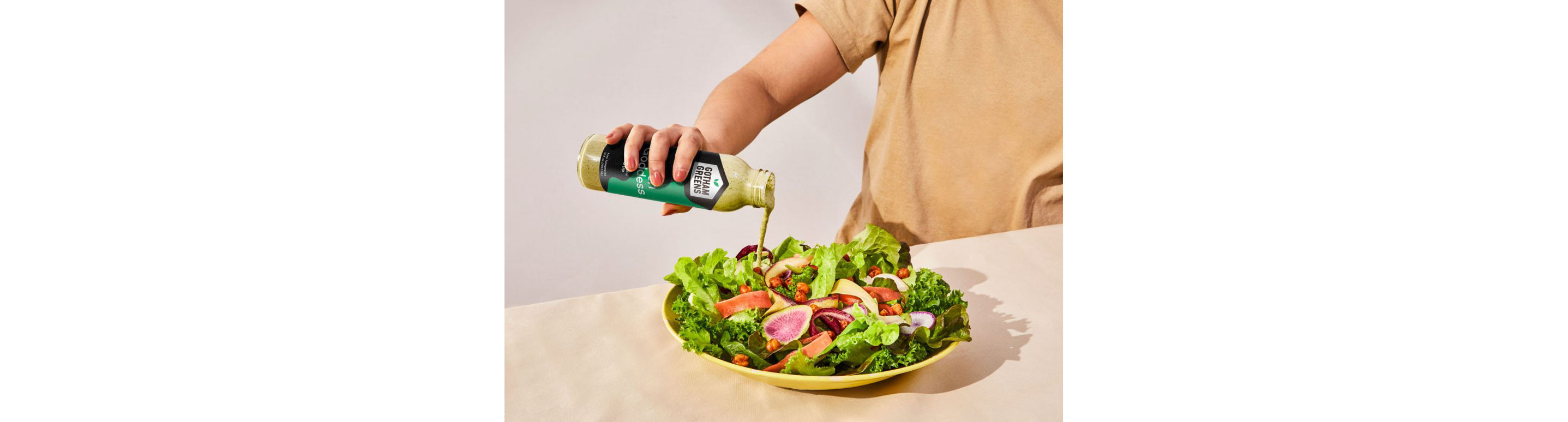 A person pouring dressing on a salad.