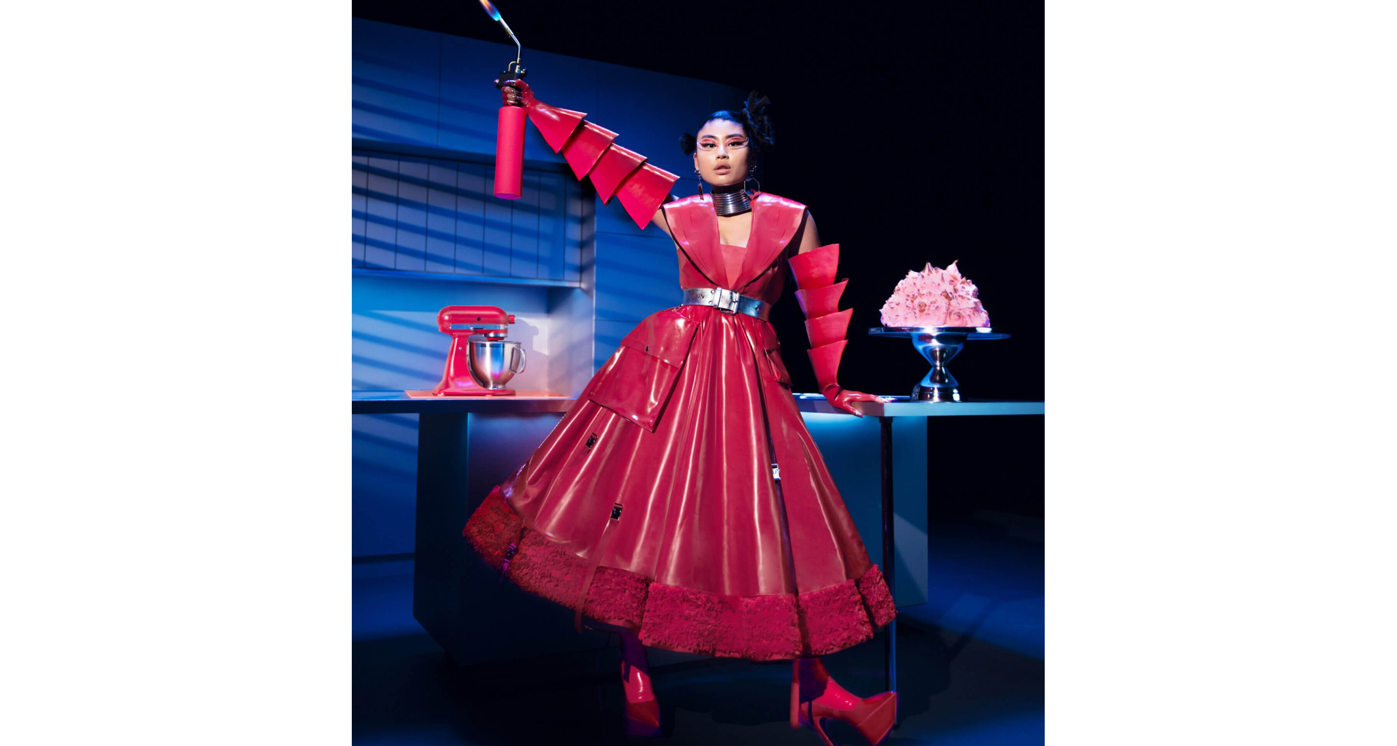 A model posing in a kitchen wearing Look Seven while holding a lit blow torch near a toasted meringue dessert.