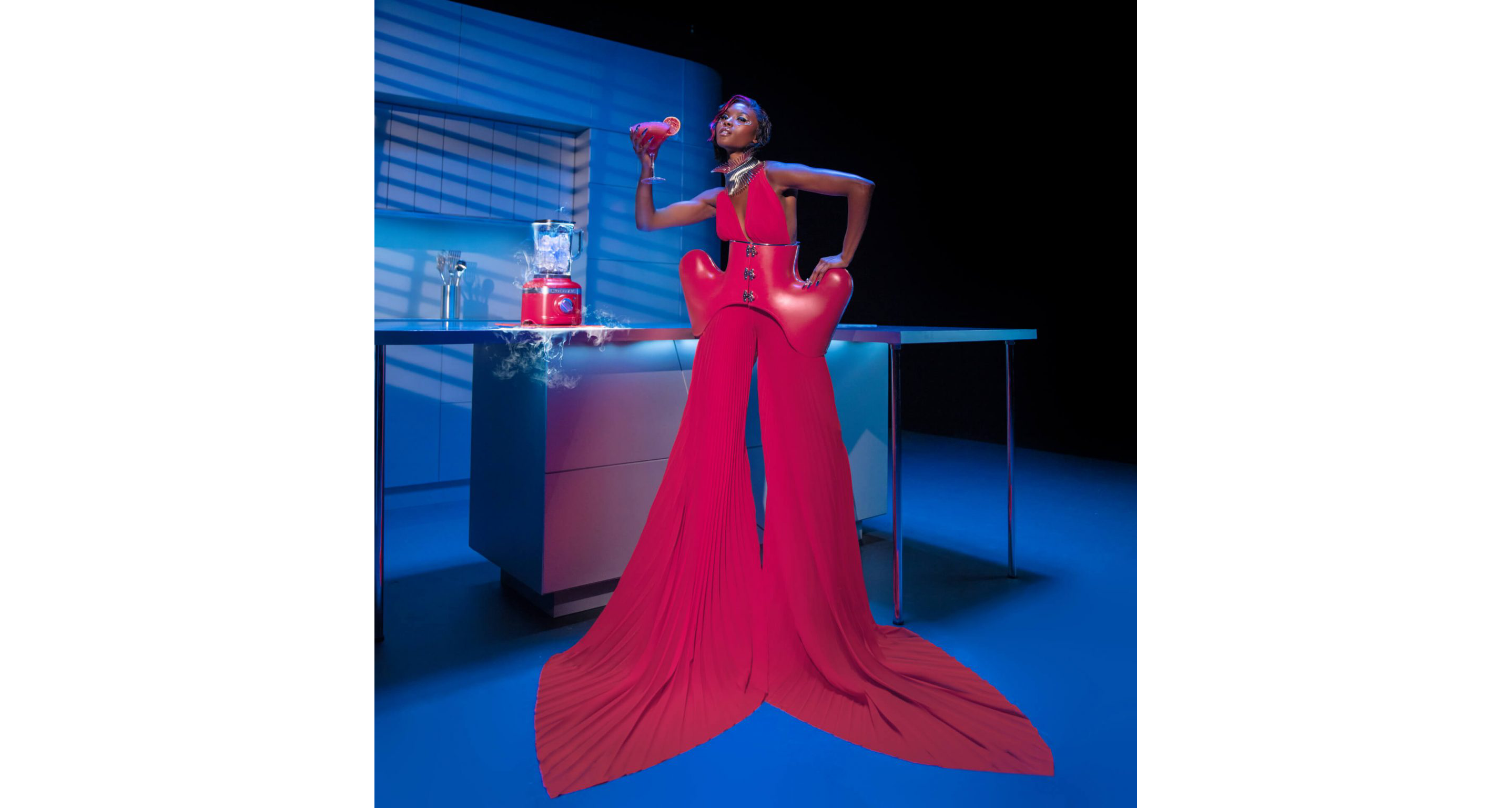 A model dressed in one of Marta Del Rio’s Hibiscus Collection looks posing with the blender and a mixed drink.