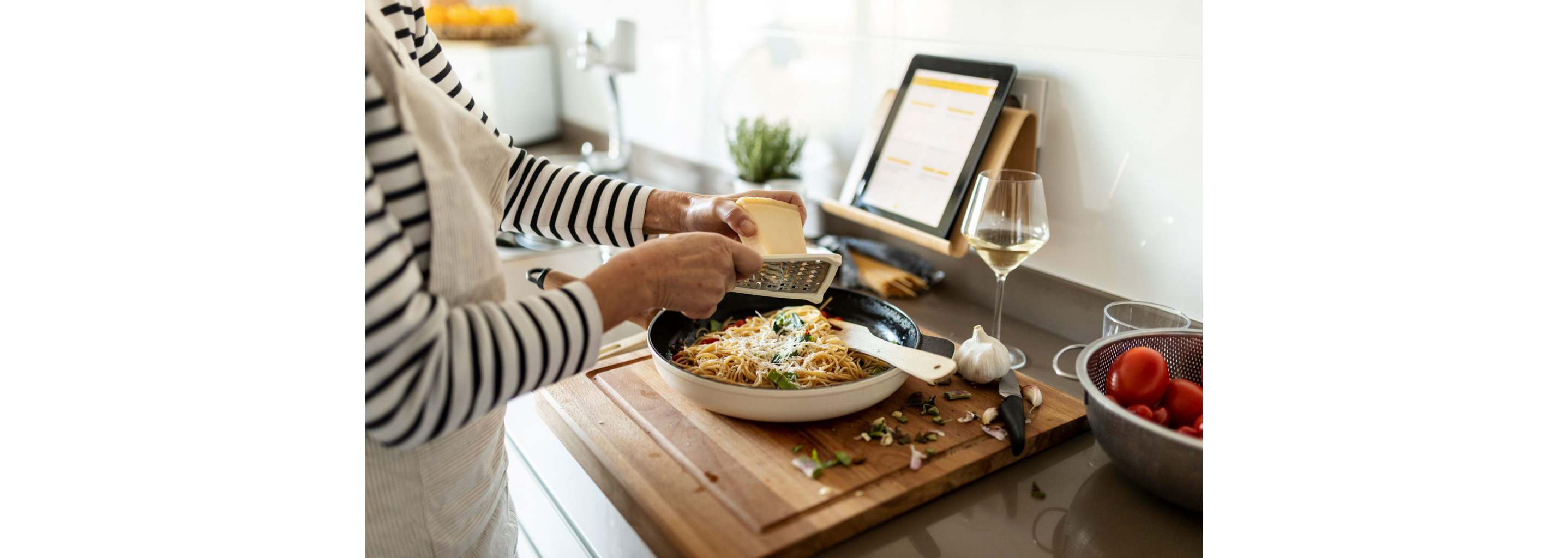 A person grating parmesan cheese into a skillet filled with spaghetti.