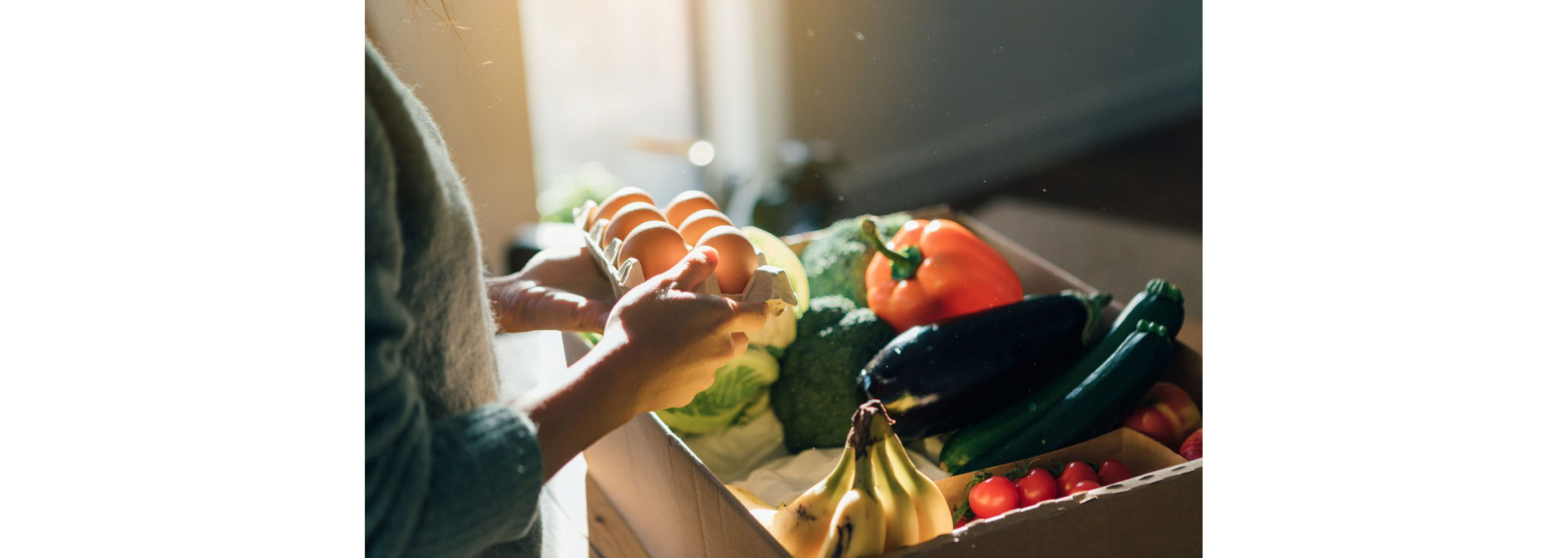 A person sorting through a carton of eggs and fresh produce.
