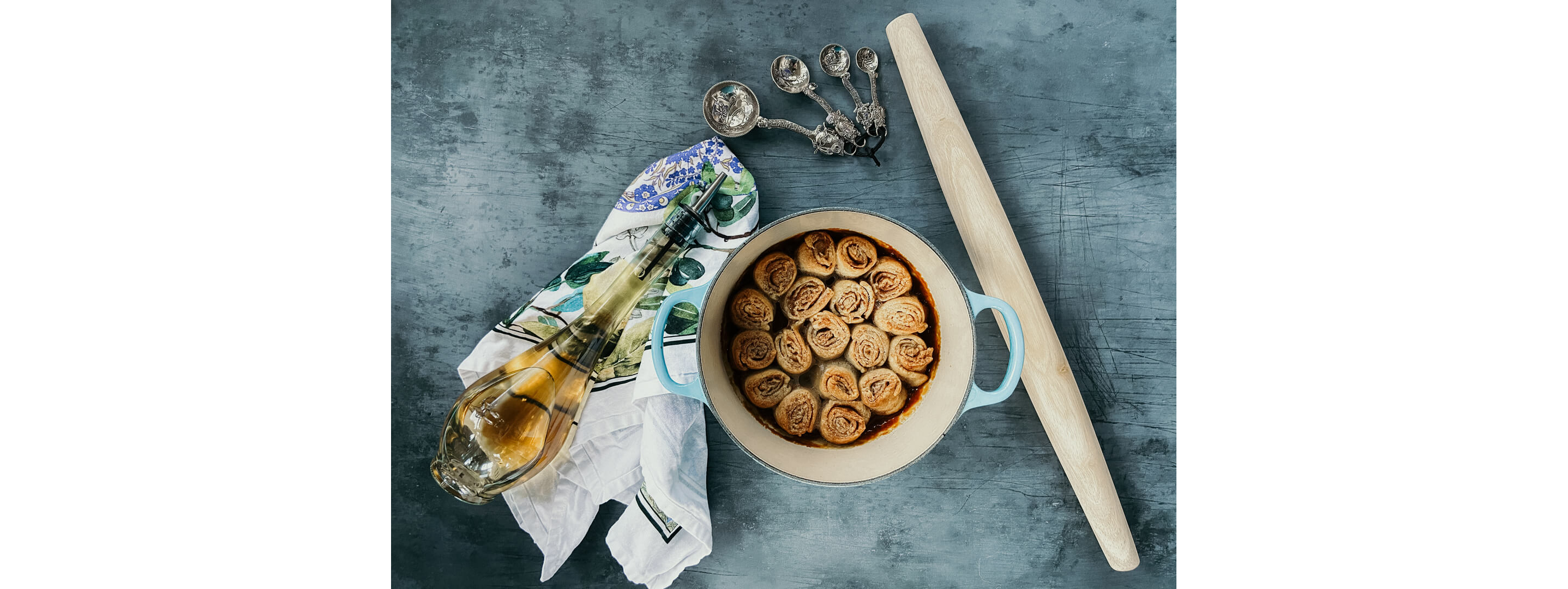 A light blue dutch oven holding cinnamon rolls next to a bottle of vinegar on a delicate towel.