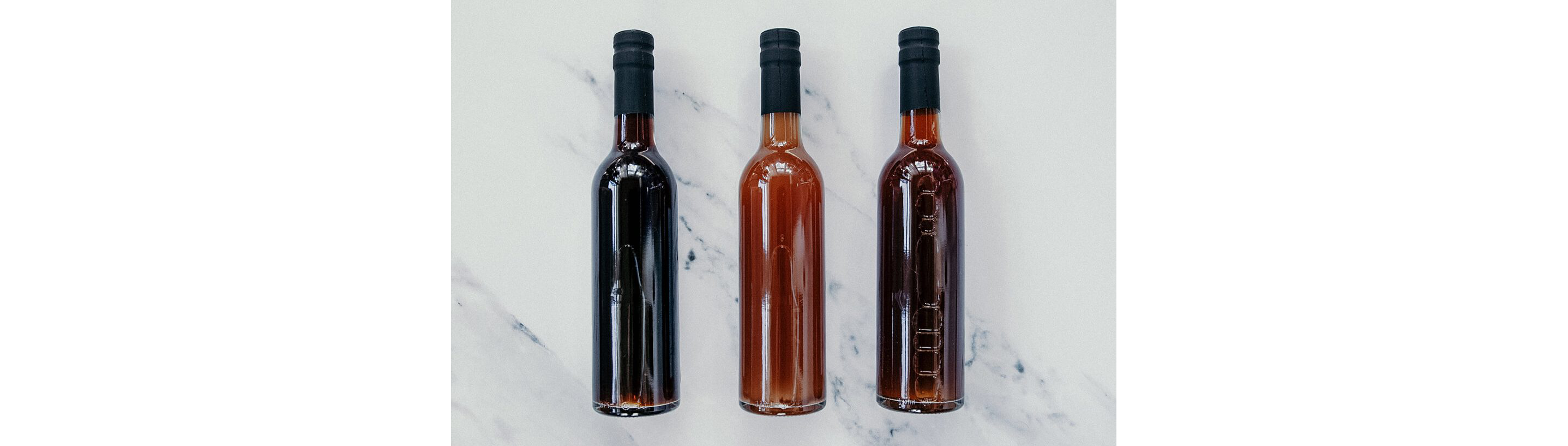 Three bottles of varying shades of brown holding vinegar.