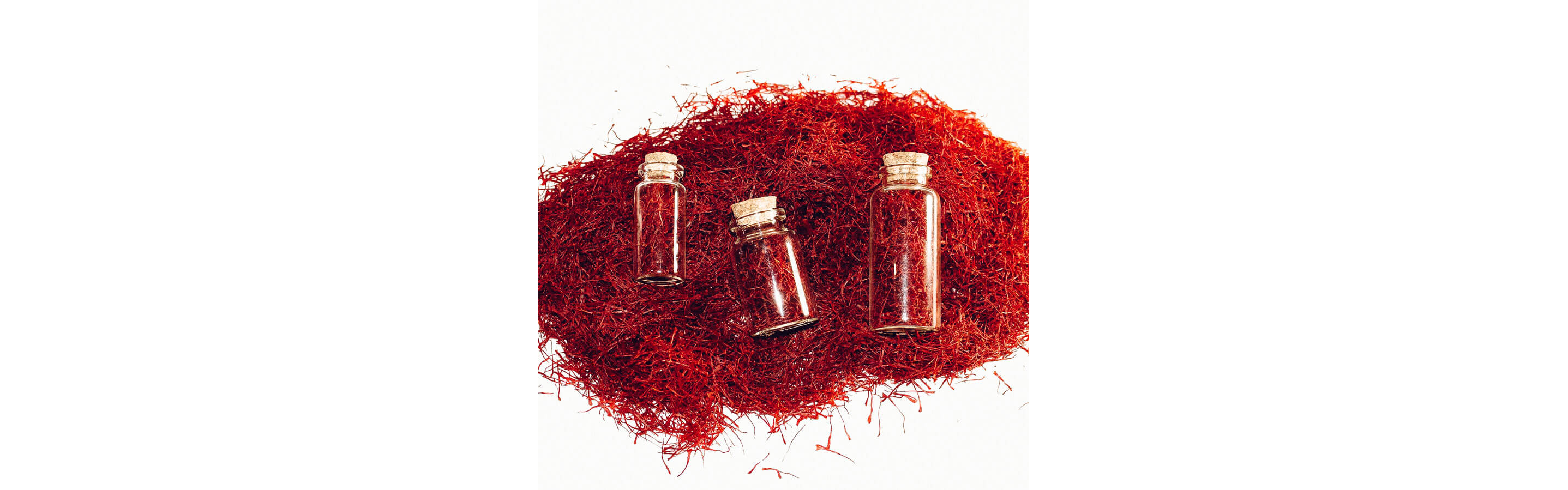 Three small, corked bottles of saffron resting on a pile of saffron.
