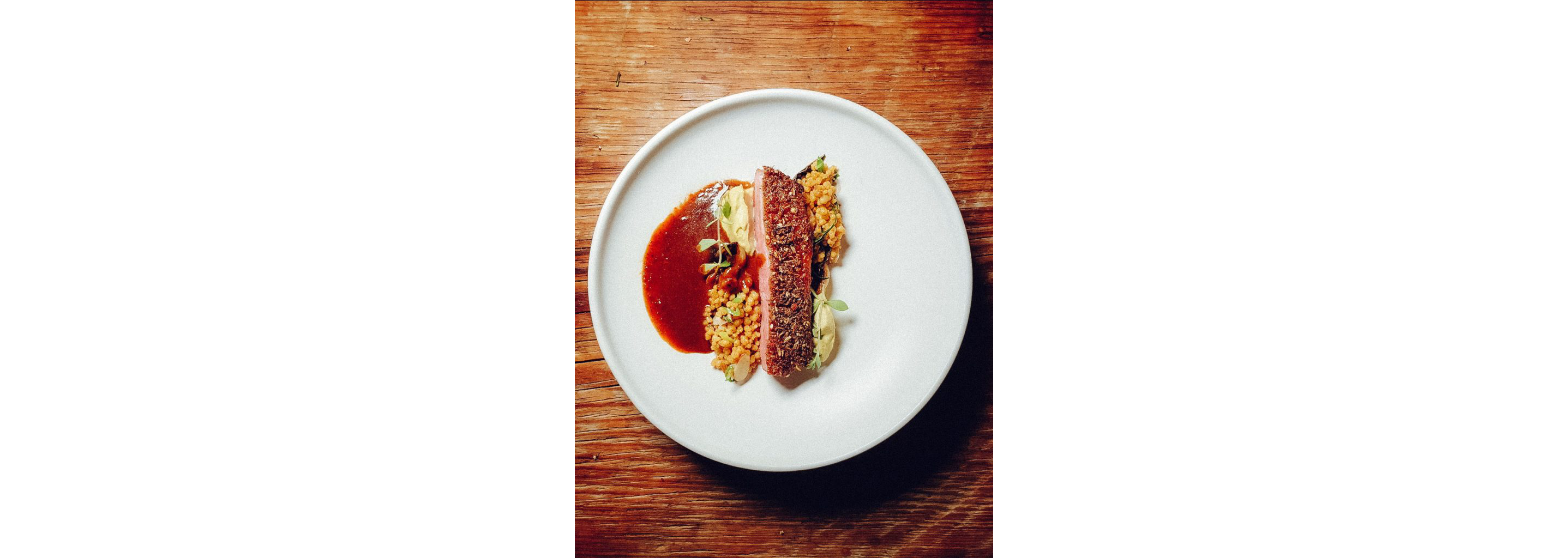 A slice of seared duck resting a bed of cous cous with sauce.
