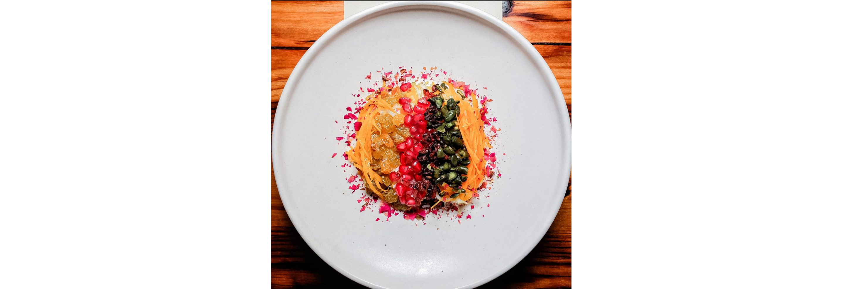 Pomegranate seeds, dried fruits, nuts and other delicacies served on a white plate.