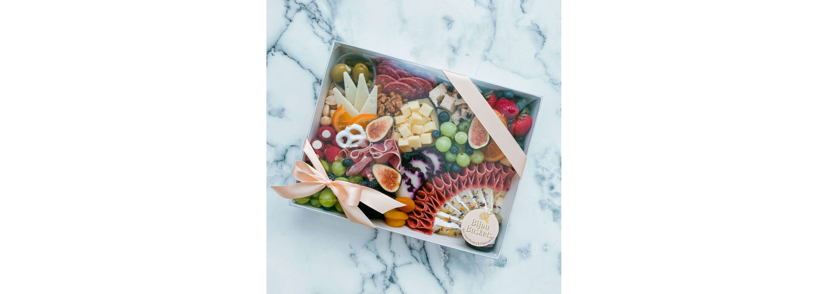 A picnic box filled with a variety of fruits, cheeses and nuts.