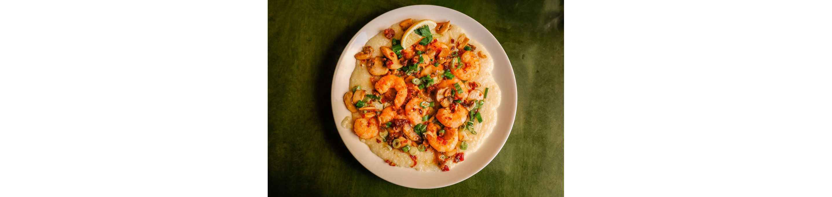 A large, flat bowl filled with shrimp and grits.