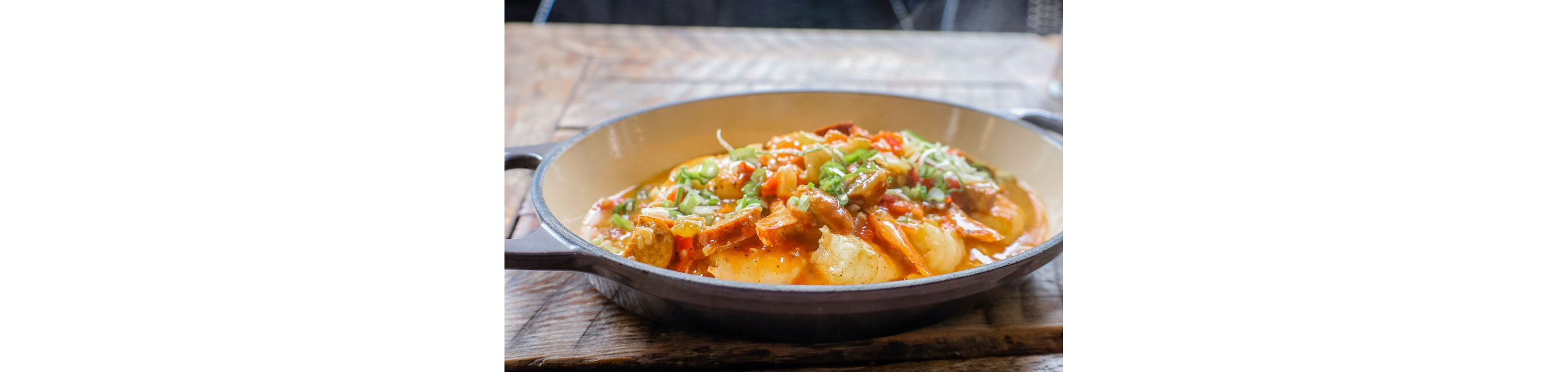 An oval dish filled with steaming cajun shrimp and grits.