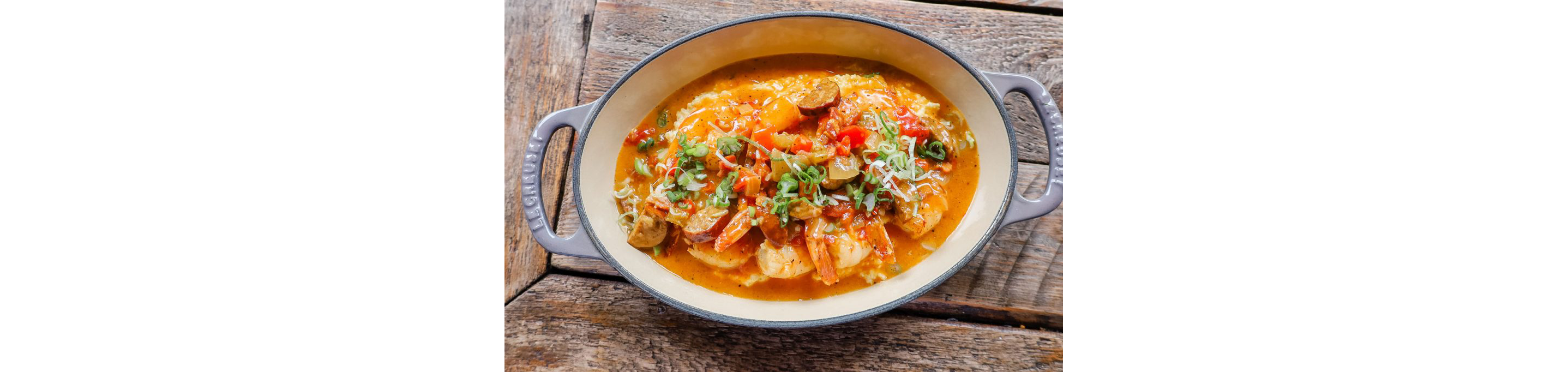 An overhead shot of an oval dish filled with cajun shrimp and grits.