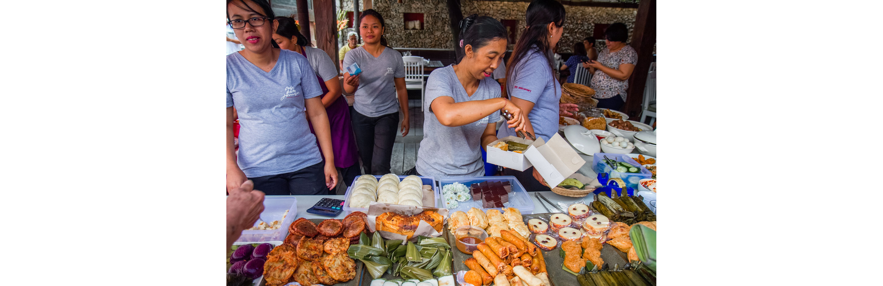 Women gently packing Indonesian desserts into a white carryout box.