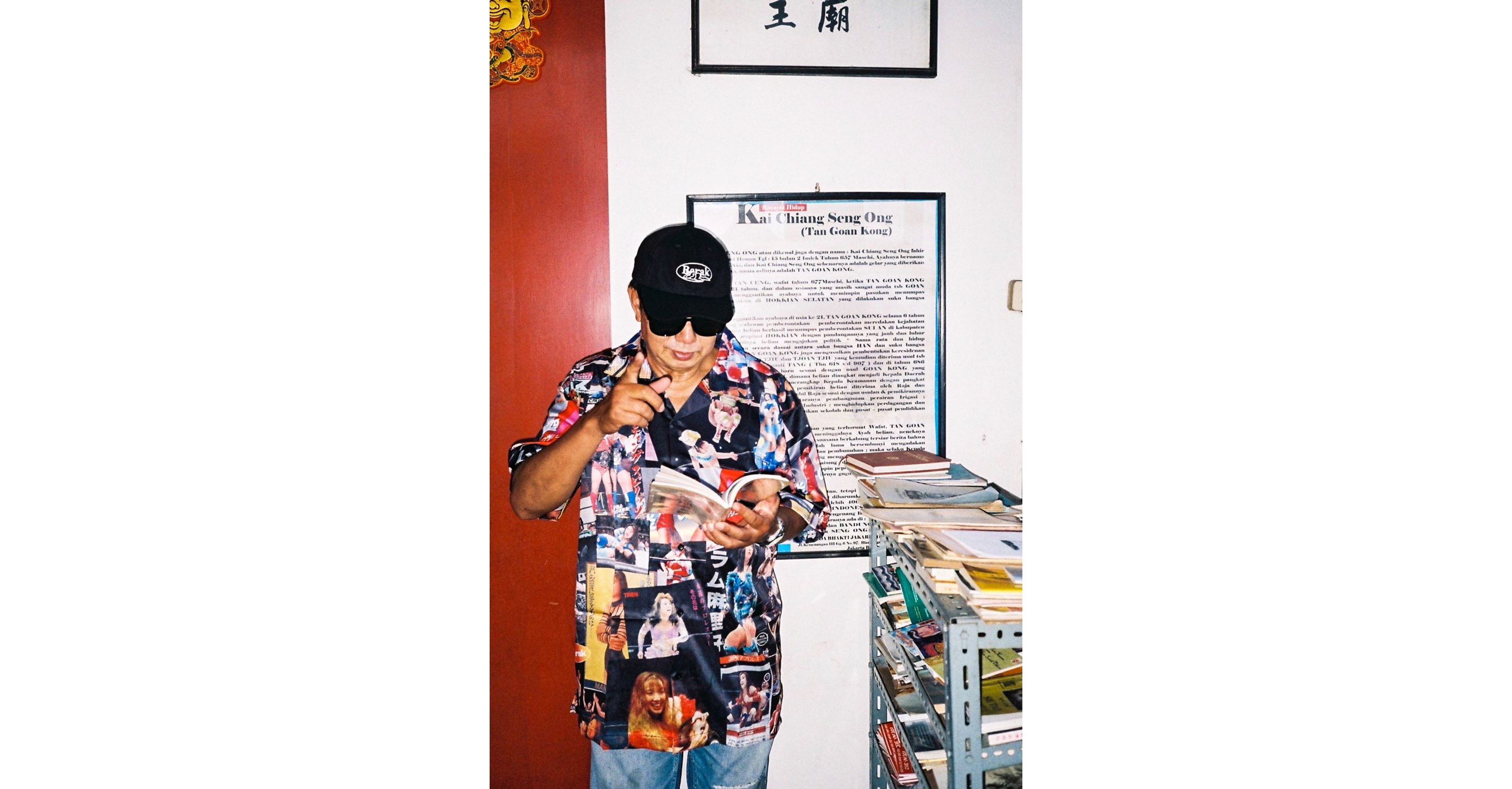 Paulus Supomo in a retro shirt and sunglasses reading a magazine.