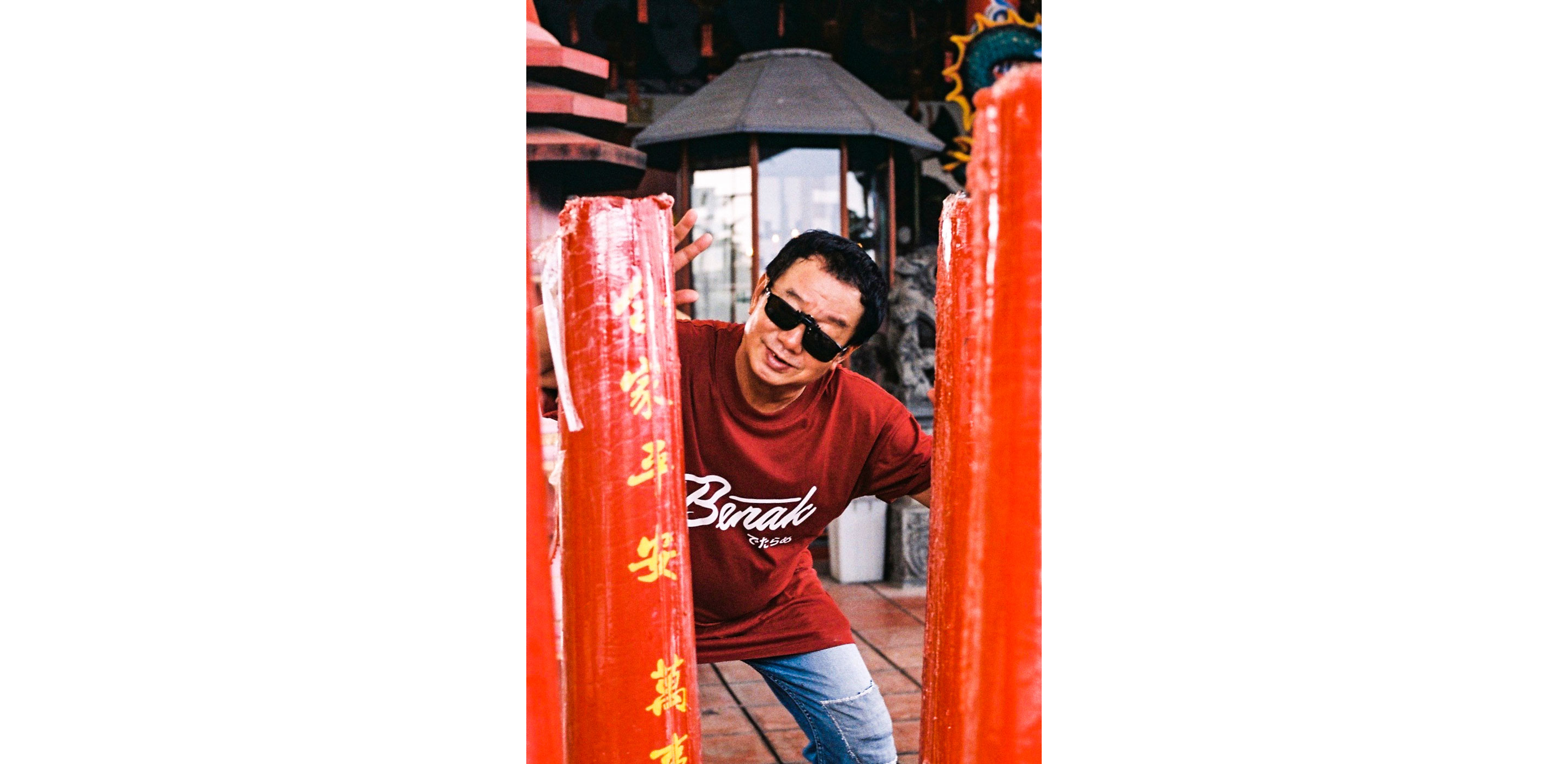 Paulus Supomo in sunglasses posing behind red pillar with yellow Chinese lettering on the street.