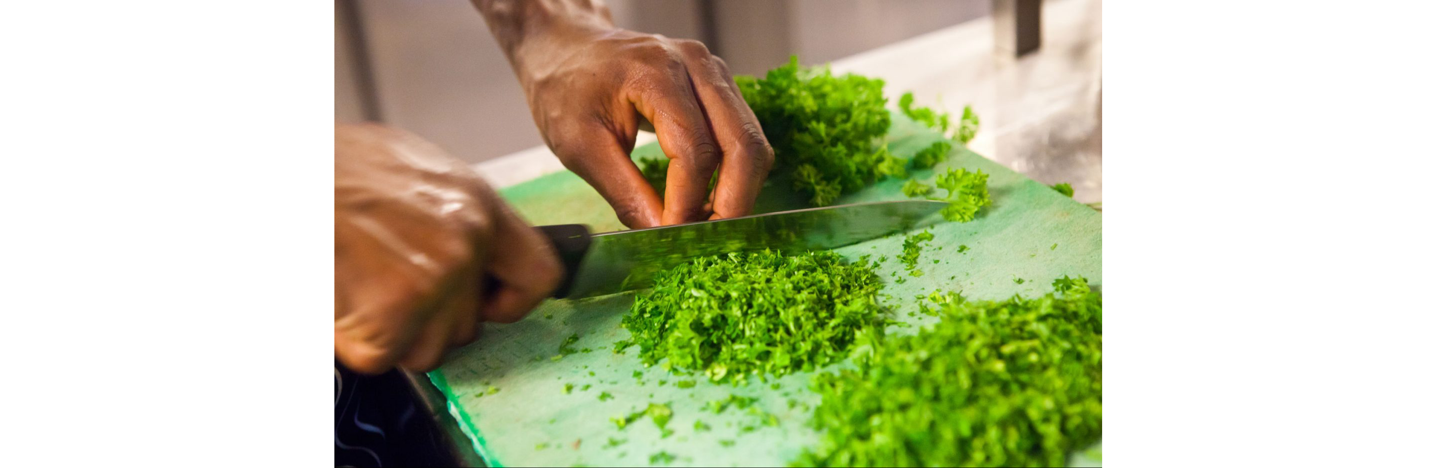 A person chopping herbs on a green cutting board.