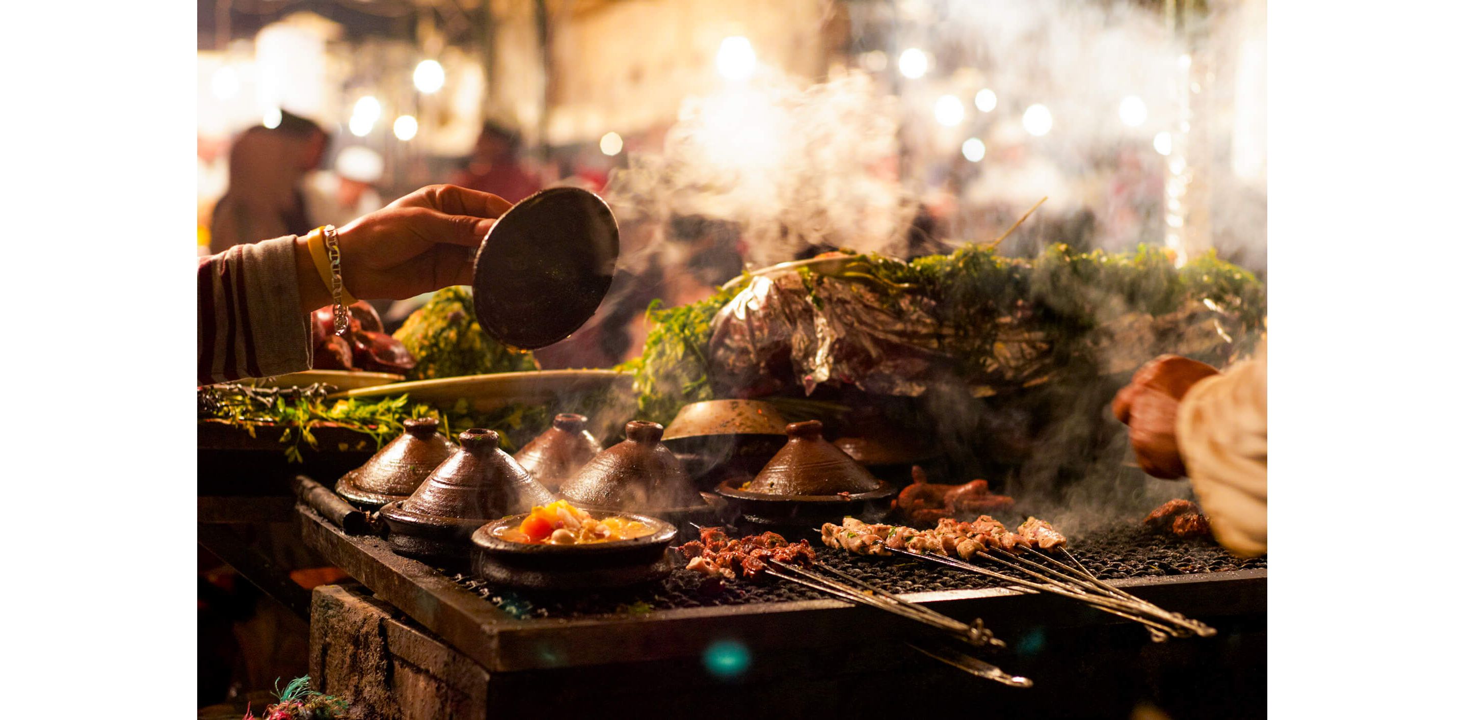 A woman checking her tagine pots as they sit on a large grill with various meats and kebabs.