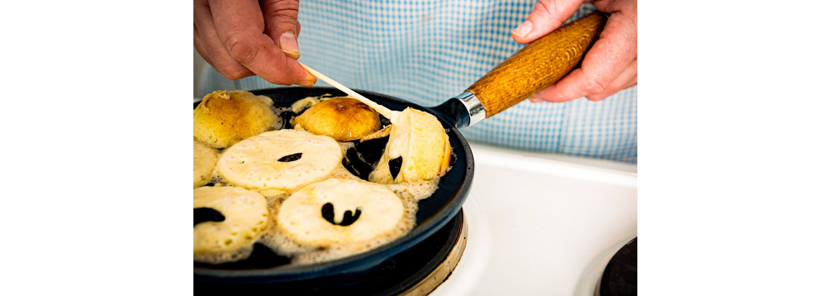 A person using an aebleskiver pan to make Danish pancake balls.