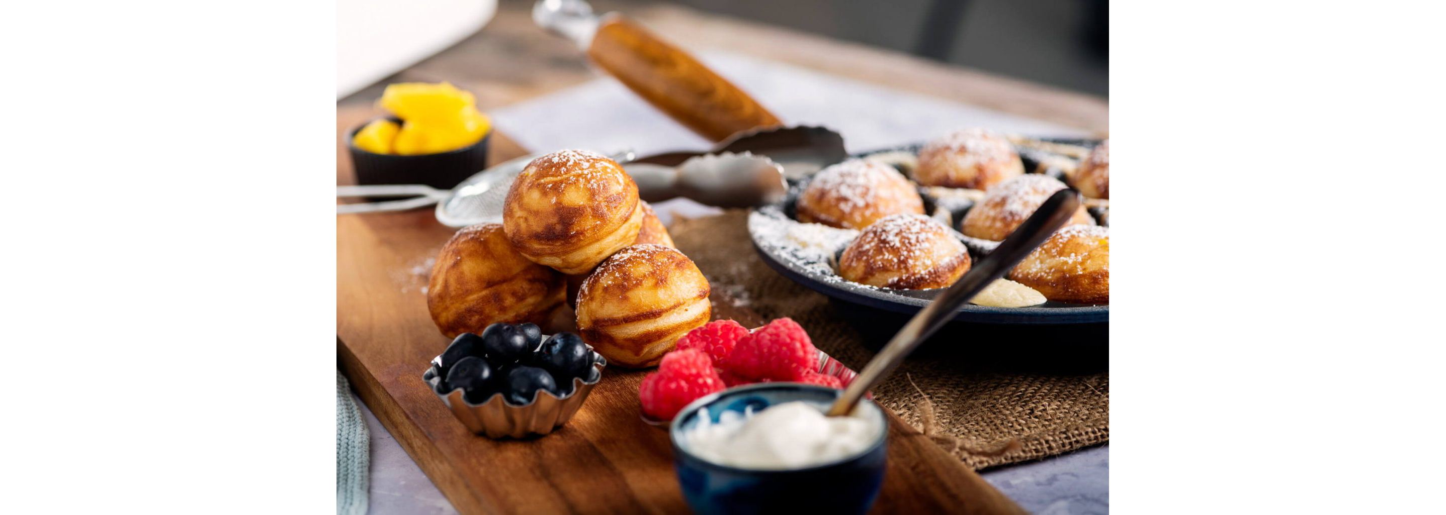 Danish pancake balls topped with powdered sugar and accompanied by a variety of fresh berries.