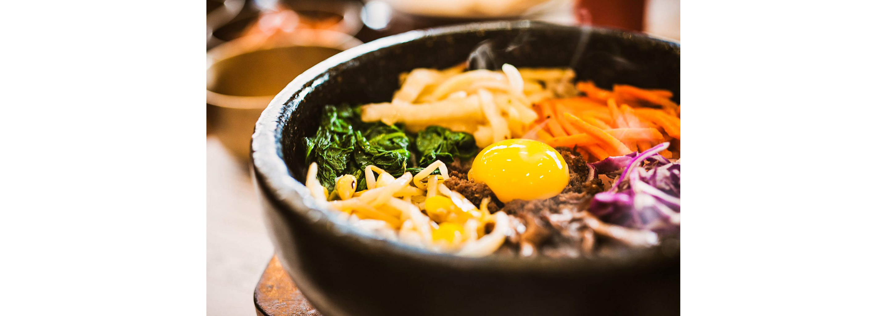 A dolsot bowl filled with bibimbap, a layer of rice topped with meats, veggies and an over-easy egg.