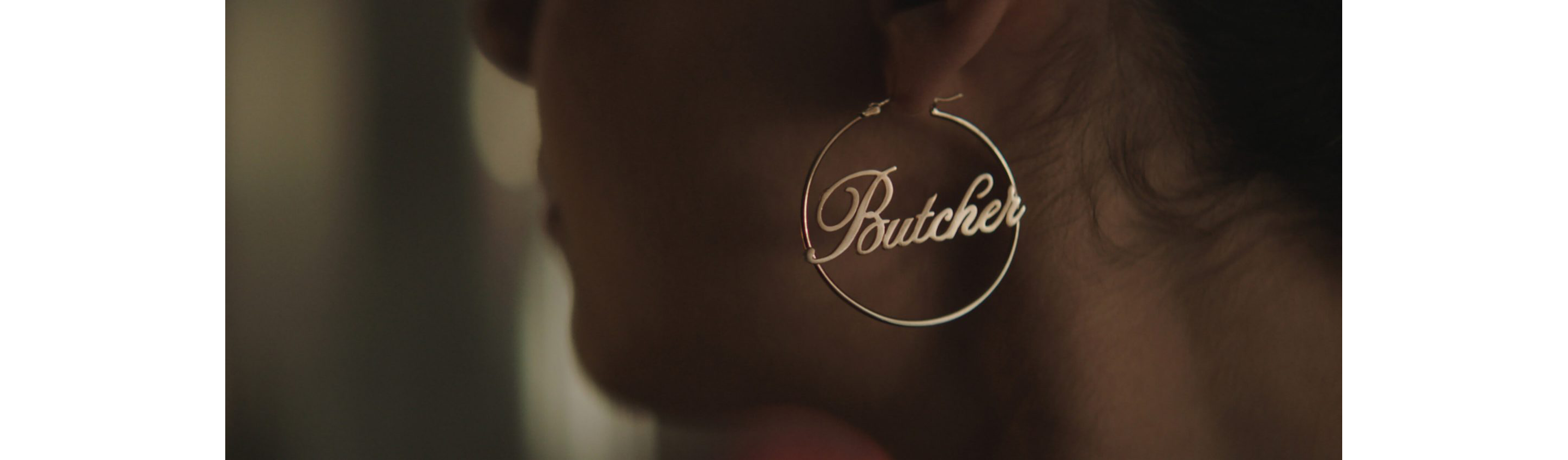A gold hoop earring with the word Butcher spelled out in center.