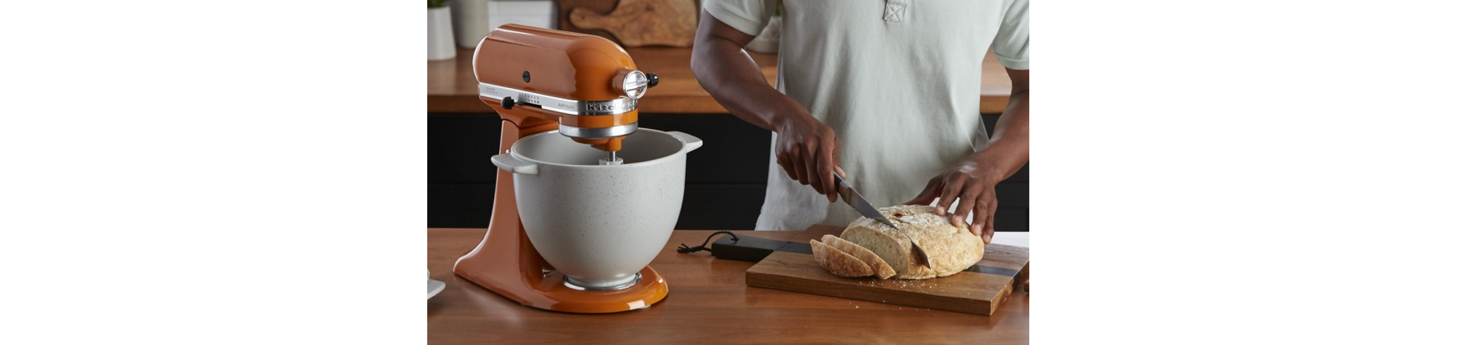 A person slicing bread next to a KitchenAid® stand mixer.