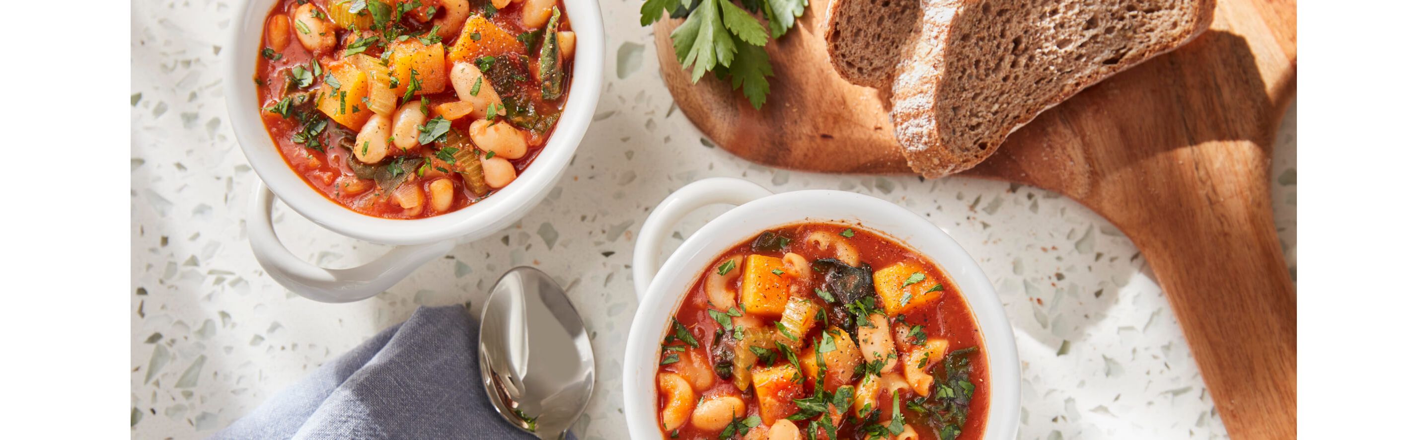 Two bowls of Pasta Fagioli sitting next to dark rye bread