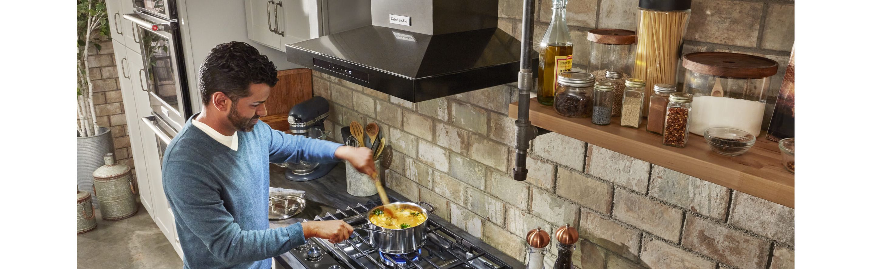 Person stirring food on a range with a KitchenAid® hood above it