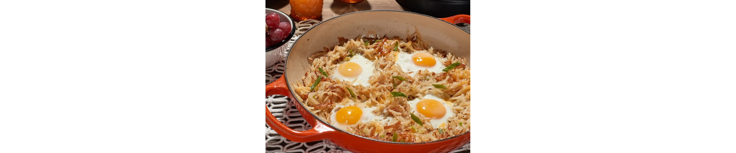 Potato hash with sunny side up eggs in red skillet