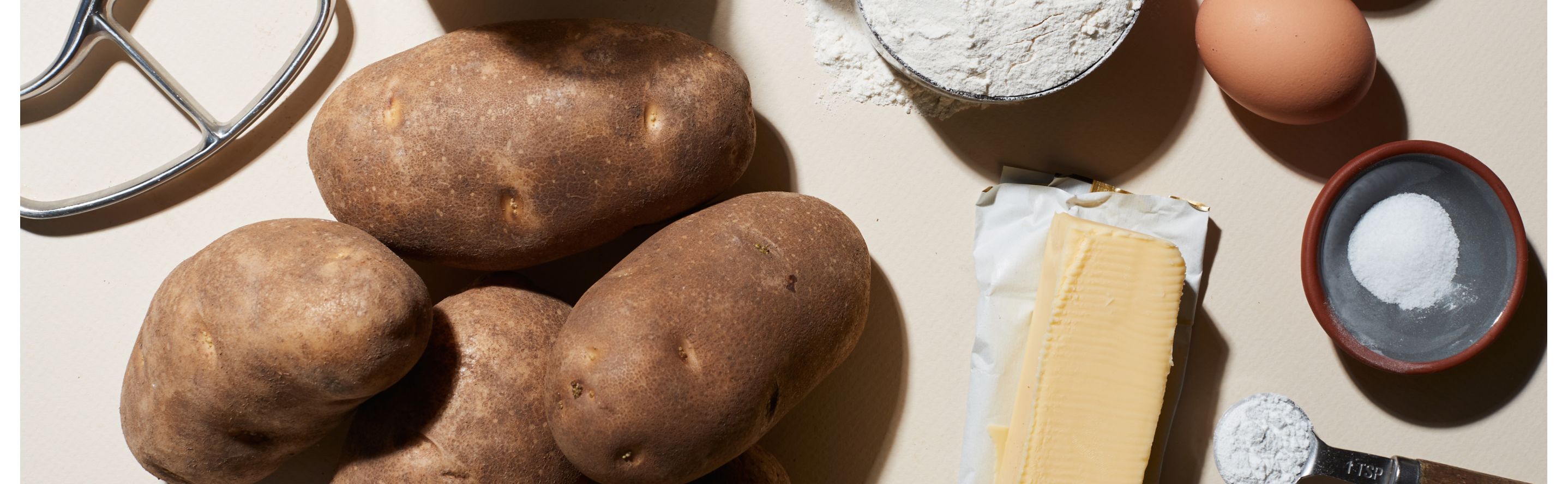 Russet potatoes on white countertop with assorted ingredients