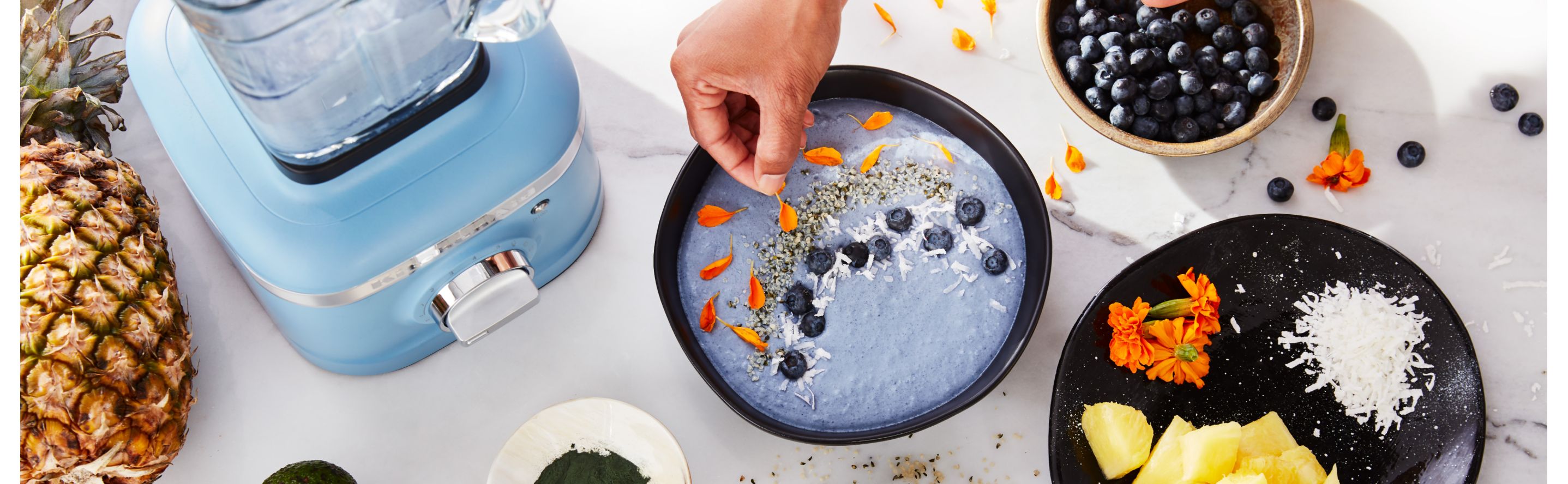 Person garnishing a blue smoothie bowl next to blue KitchenAid® blender