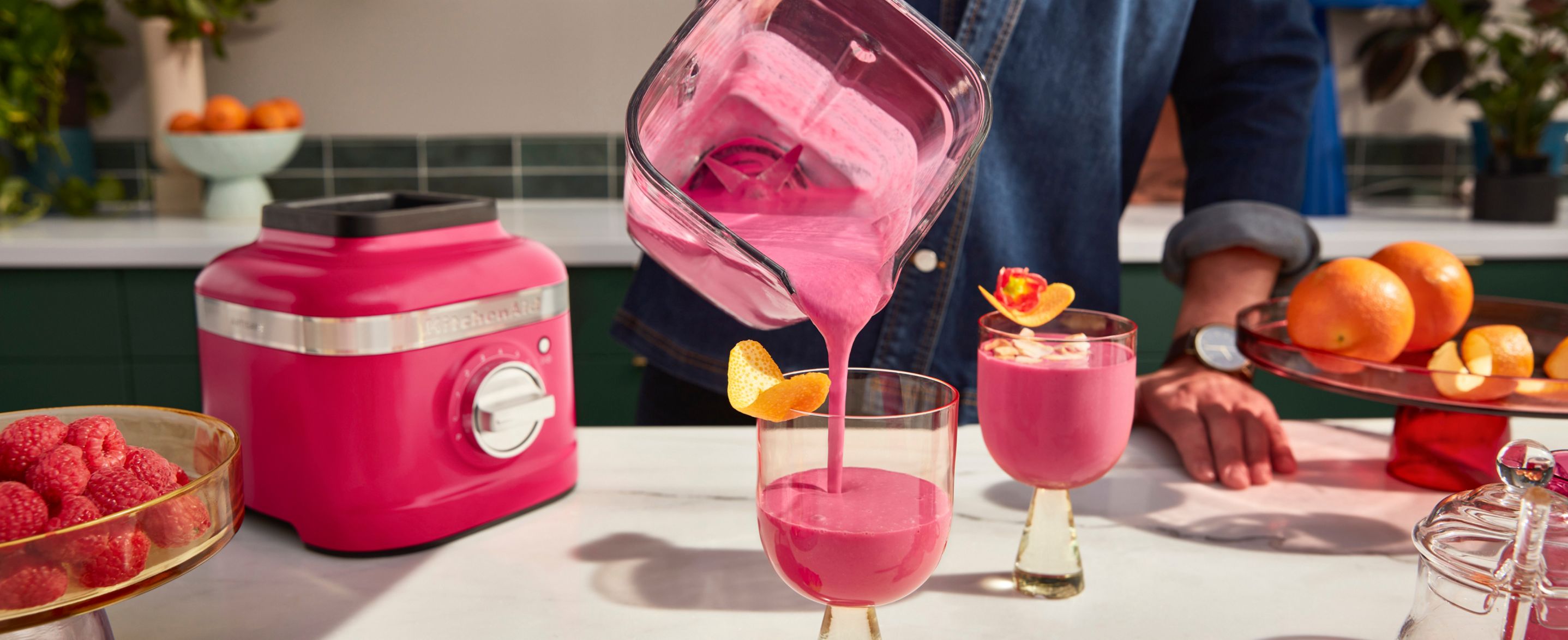 A person pouring a blended hibiscus drink into stylish cups with orange peel garnishes. 
