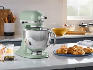 A light green KitchenAid® Stand Mixer on a white countertop with a tray of baked goods nearby