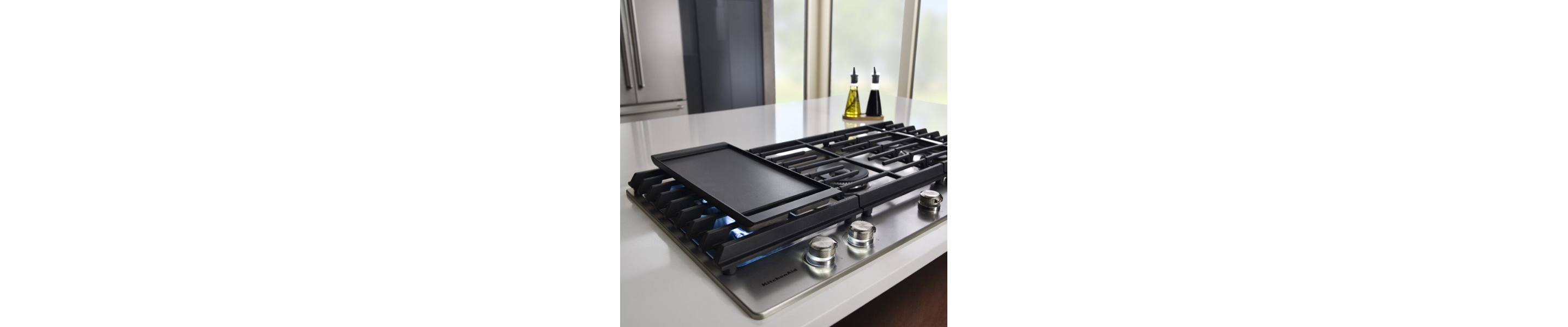 Griddle resting vertically on the left side of a gas cooktop