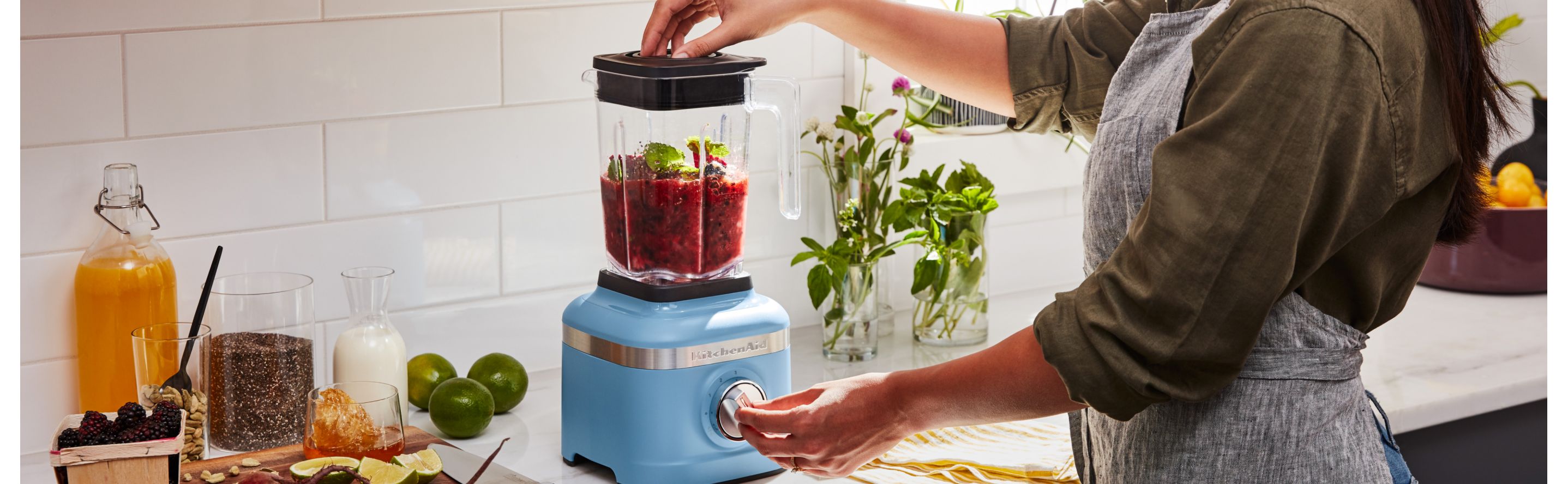 A woman blending fresh vegetables in a KitchenAid® blender in a modern kitchen.