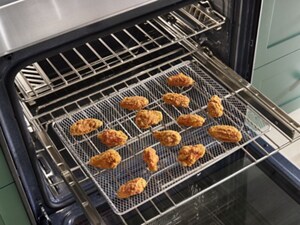 An air fryer basket full of breaded pieces of chicken sits on an open oven rack