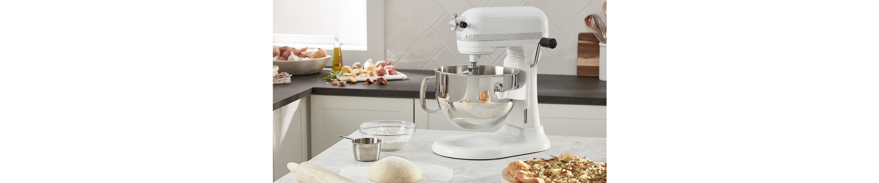 A white KitchenAid® stand mixer next to a pizza