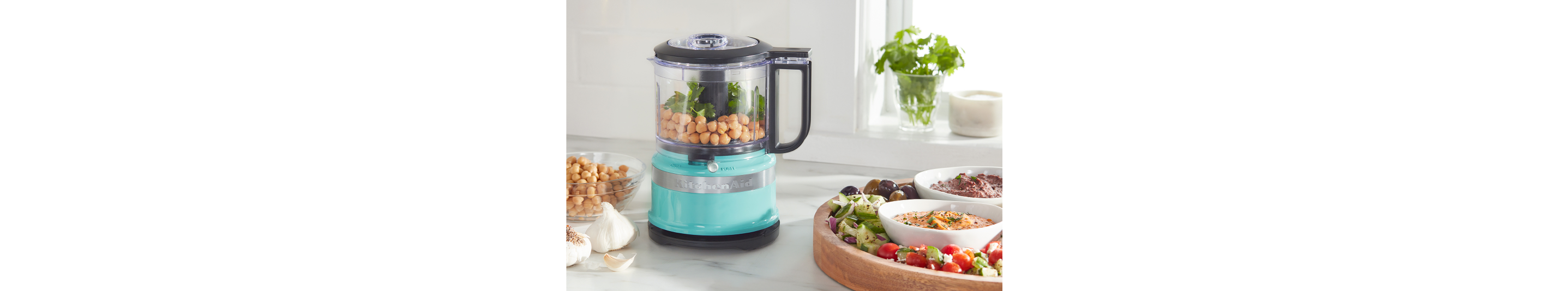 A KitchenAid® food processor next to veggies and hummus.
