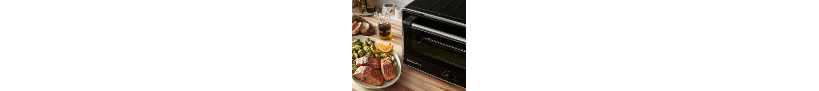 Salmon on a plate with Brussels sprouts and orange wedges next to a KitchenAid® countertop oven