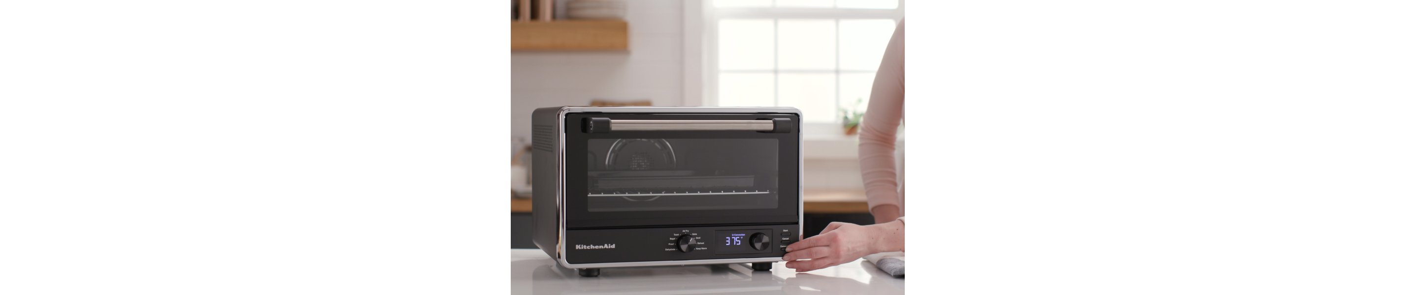 A woman programming a KitchenAid® countertop oven with air fry.