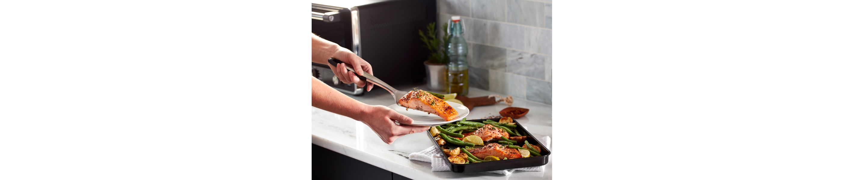 A woman putting freshly baked air fryer salmon on a plate next to a KitchenAid® countertop oven.