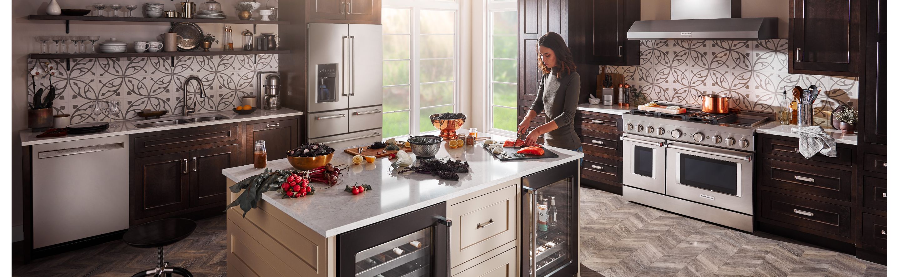 A person making a meal in a modern kitchen next to a KitchenAid® refrigerator.